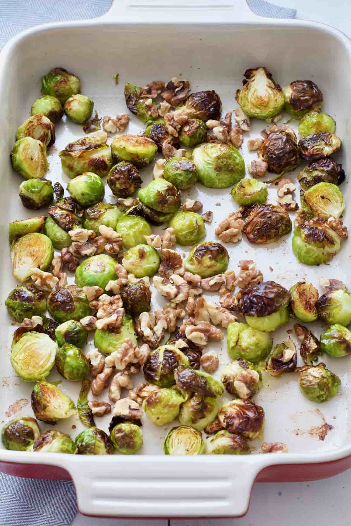 Roasted brussels sprouts in a roasting dish with added walnuts.