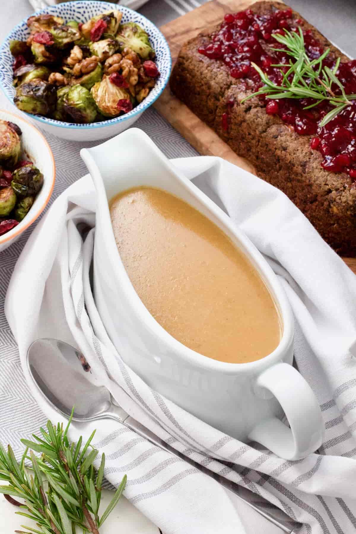 Top view of gravy in a gravy boat, bowl with Brussel sprouts and lentil loaf.