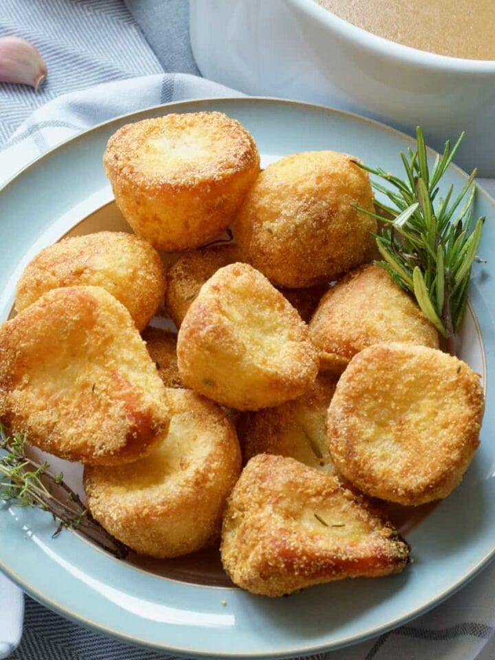 Vegan roast potatoes in a bowl with rosemary and thyme.