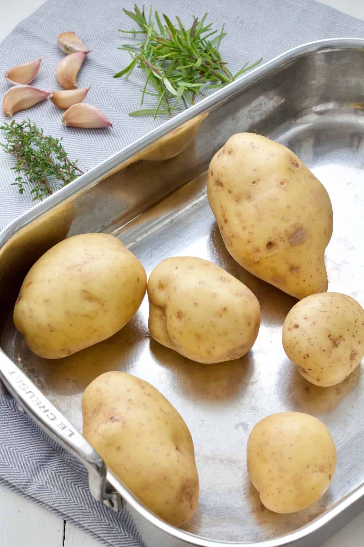 Unpeeled, raw potatoes in a tin, herbs and garlic.