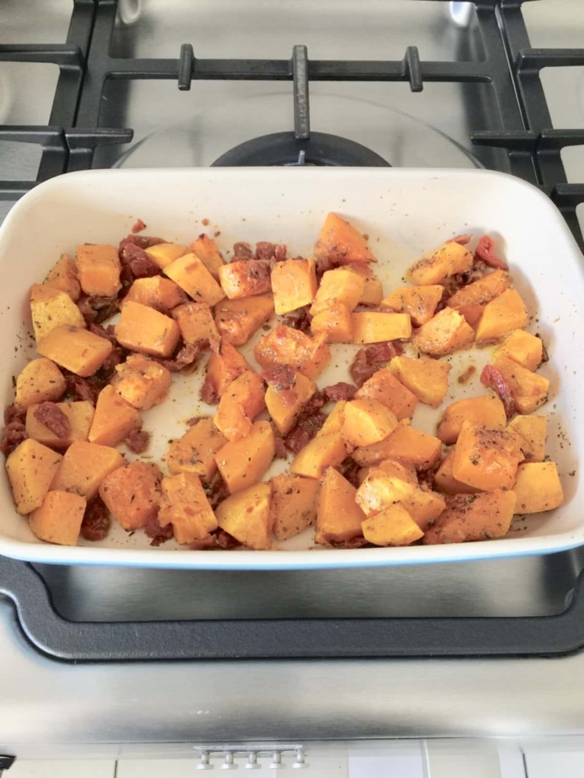 Roasted butternut squash chunks in a dish with chopped sun dried tomatoes.