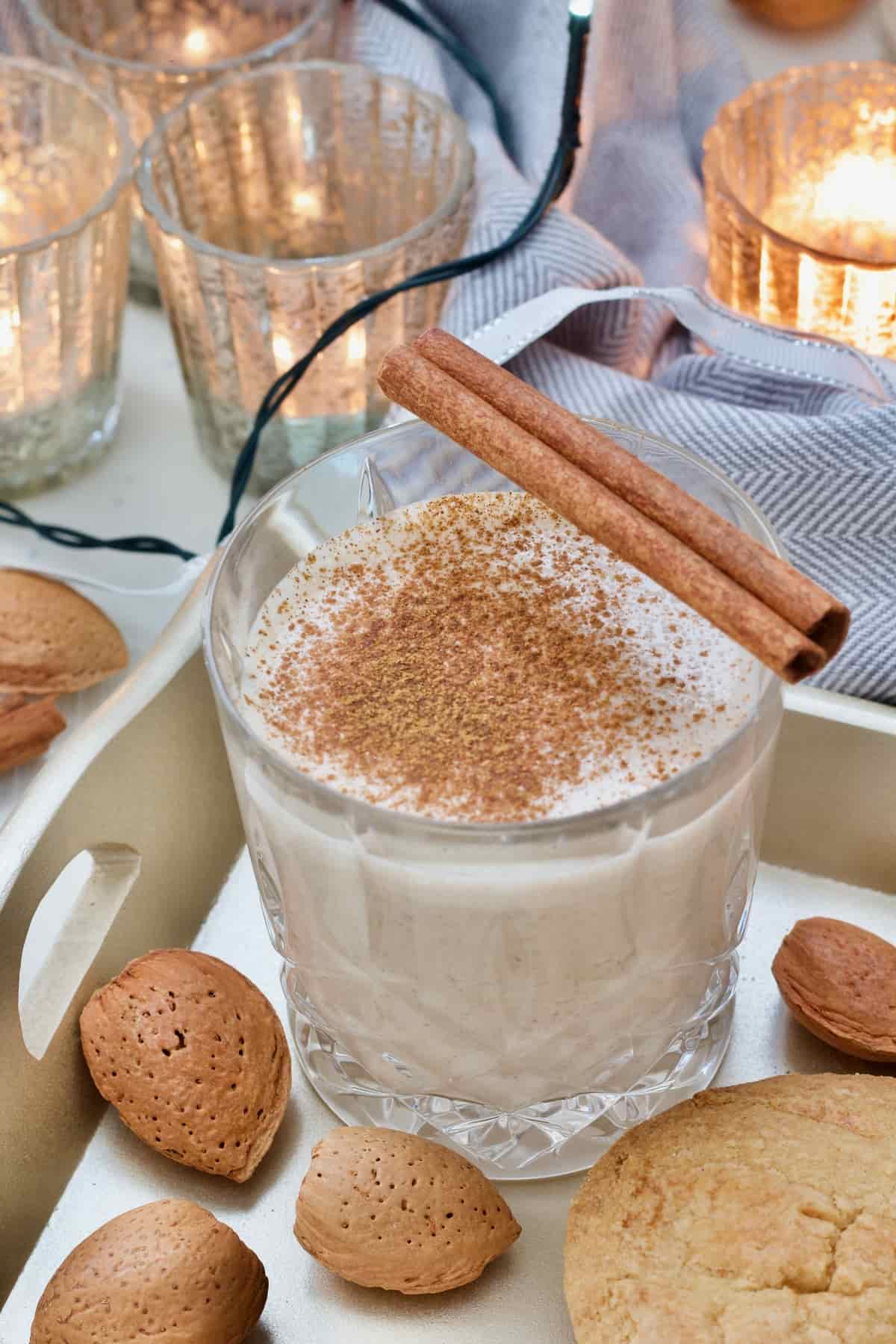 Small glass with eggnog, cinnamon stick, almonds in shells and mince pie.