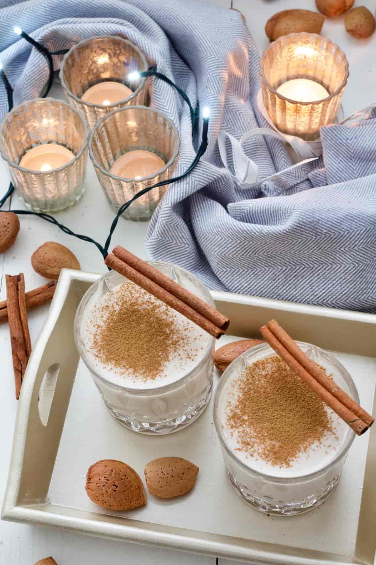 Two glasses with eggnog on a tray with tea lights in the background.