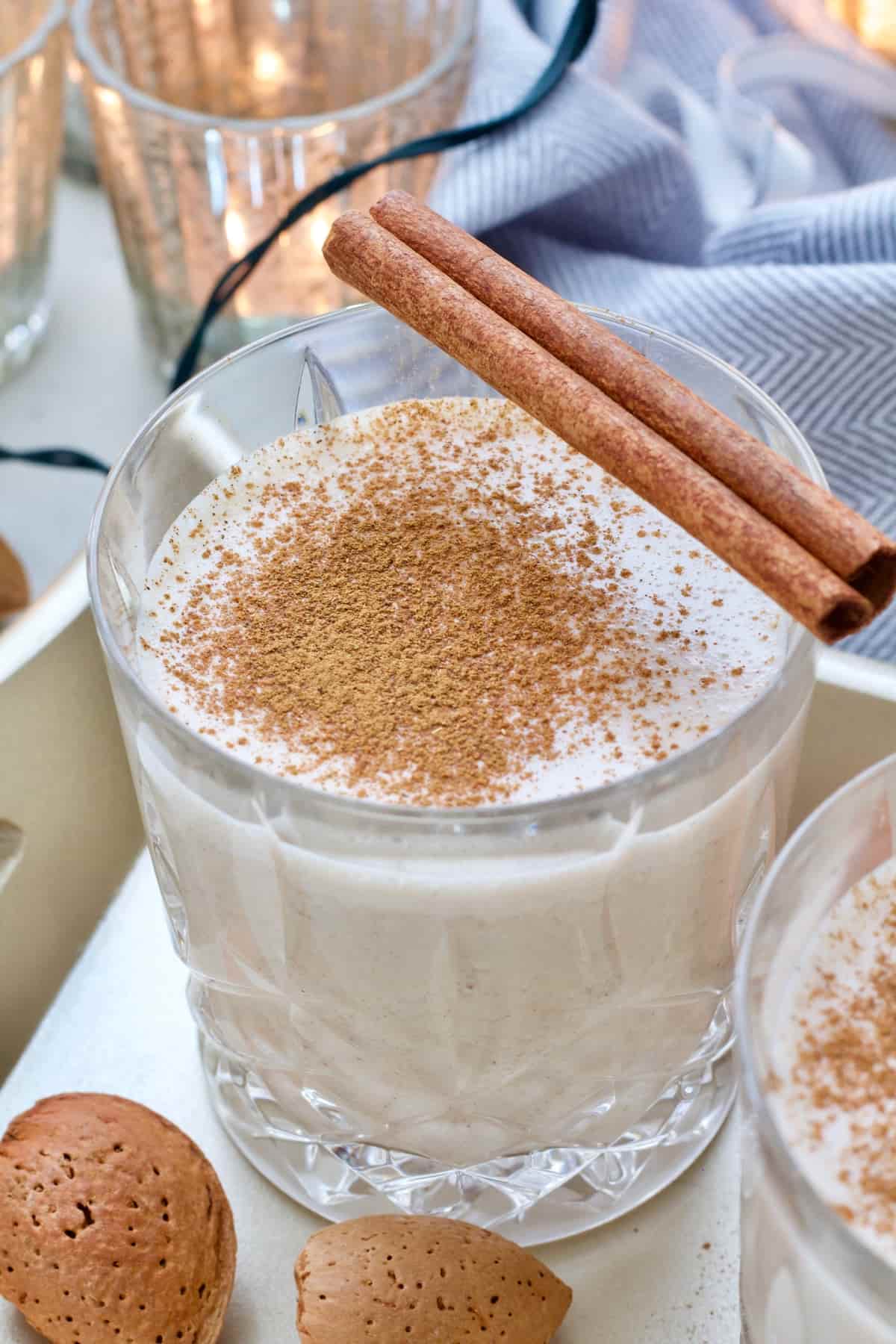 Close up of a glass with vegan eggnog, sprinkled with ground cinnamon and cinnamon stick on top.