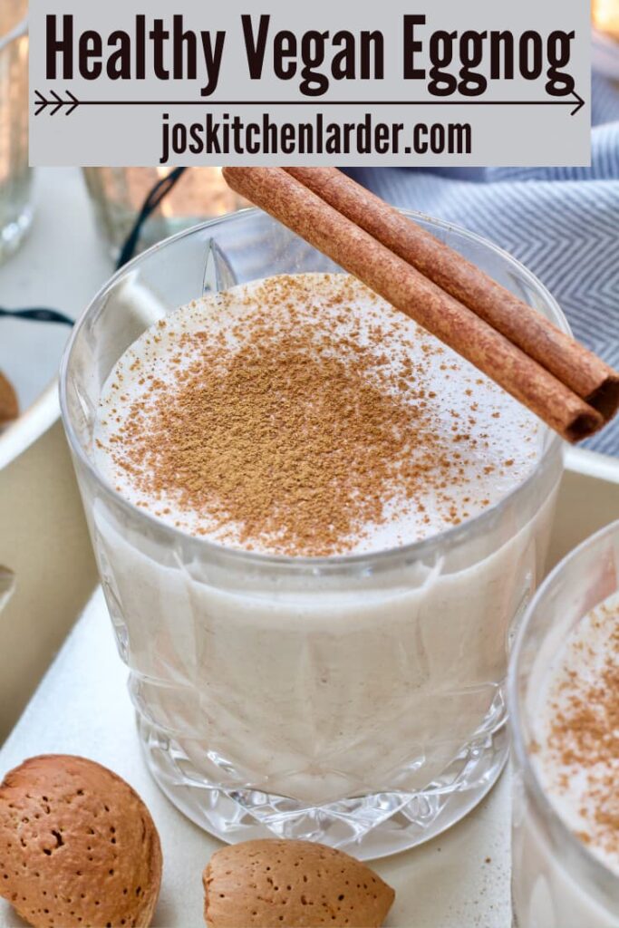 Close up of a glass with vegan eggnog, sprinkled with ground cinnamon and cinnamon stick on top.