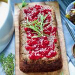 Vegan lentil loaf topped with cranberry sauce and rosemary.