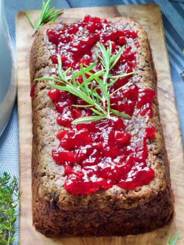 Vegan lentil loaf topped with cranberry sauce and rosemary.