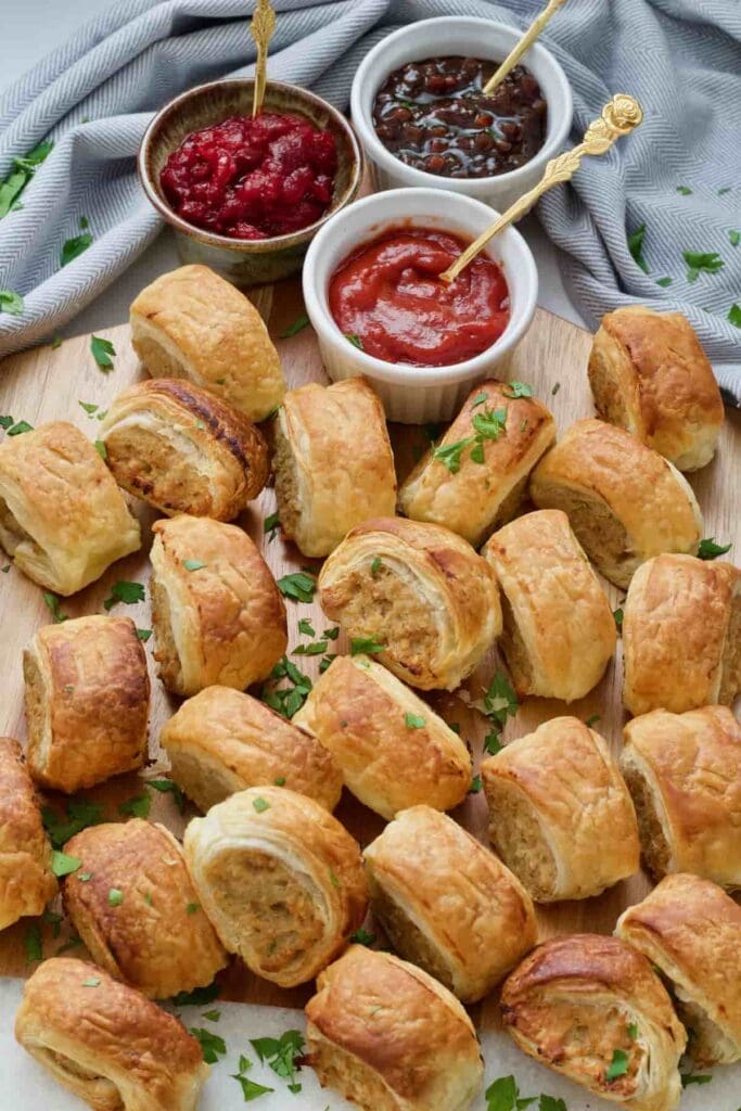Vegan sausage rolls on the board with sauces in bowls.