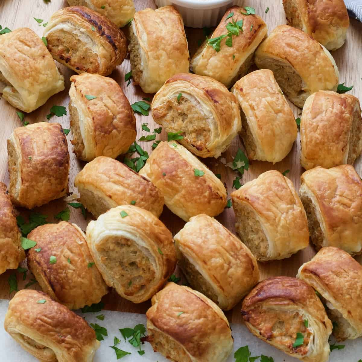 Small sausage rolls on the board sprinkled with fresh parsley.