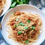 Plate with vegan spaghetti bolognese with vegan parmesan and basil garnish.