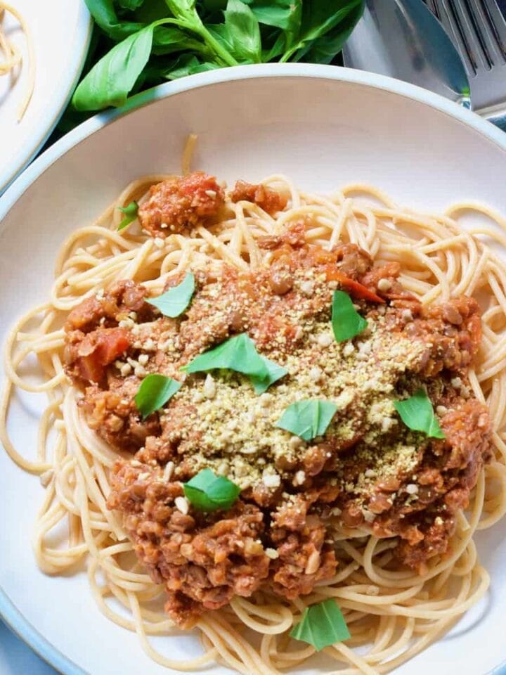 Plate with vegan spaghetti bolognese with vegan parmesan and basil garnish.