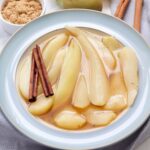 Bowl with stewed pears, cinnamon sticks and bowl with brown sugar.