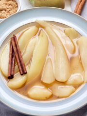 Bowl with stewed pears, cinnamon sticks and bowl with brown sugar.