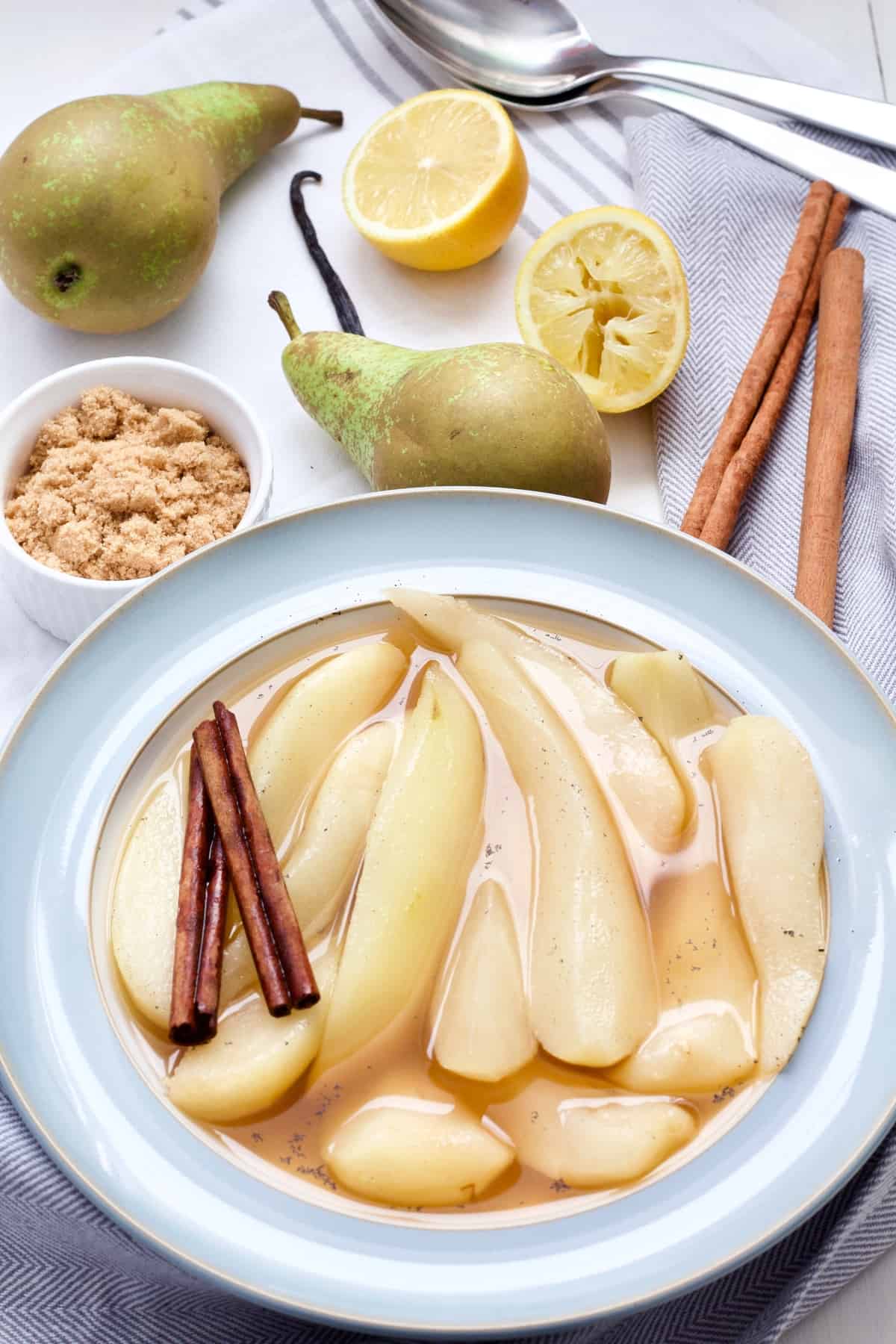Stewed pears, cinnamon sticks, sugar in a bowl, lemons & pears.