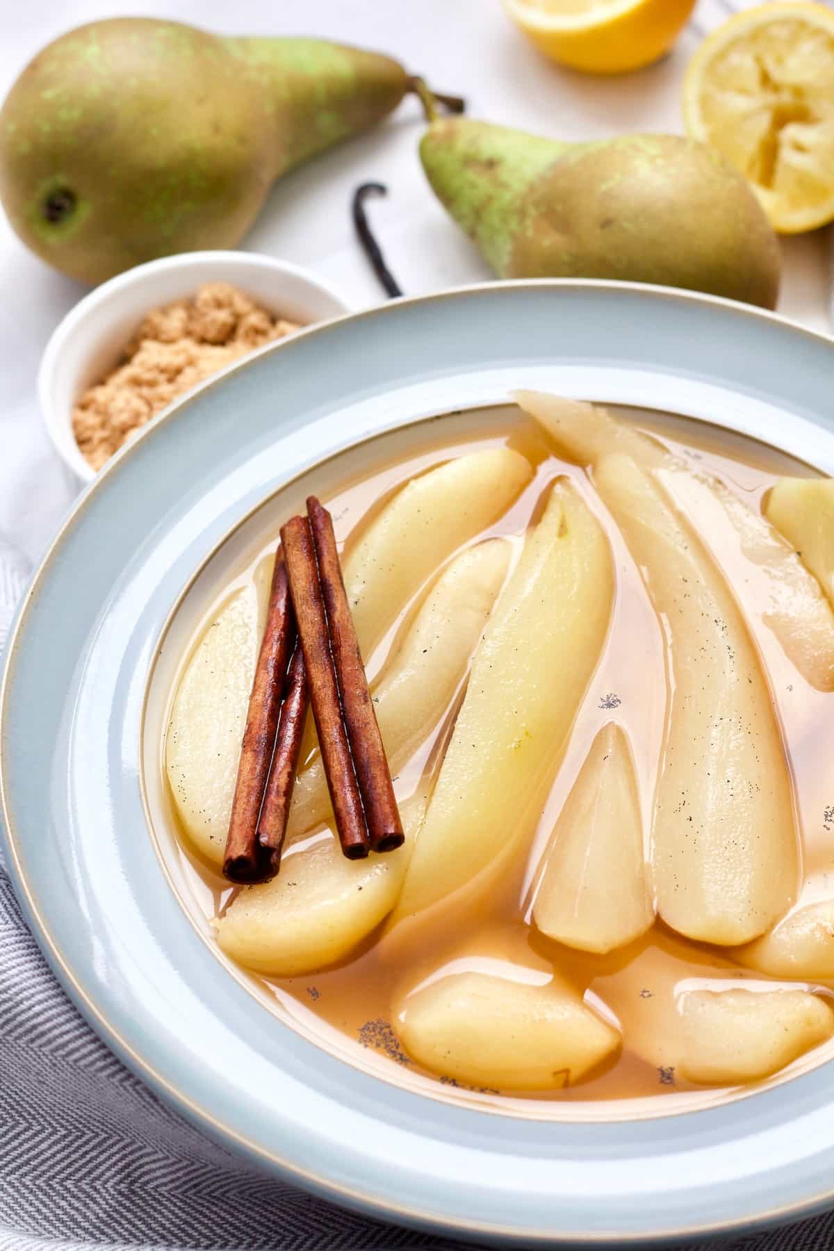 Bowl with stewed pears, cinnamon sticks, pears in the background.