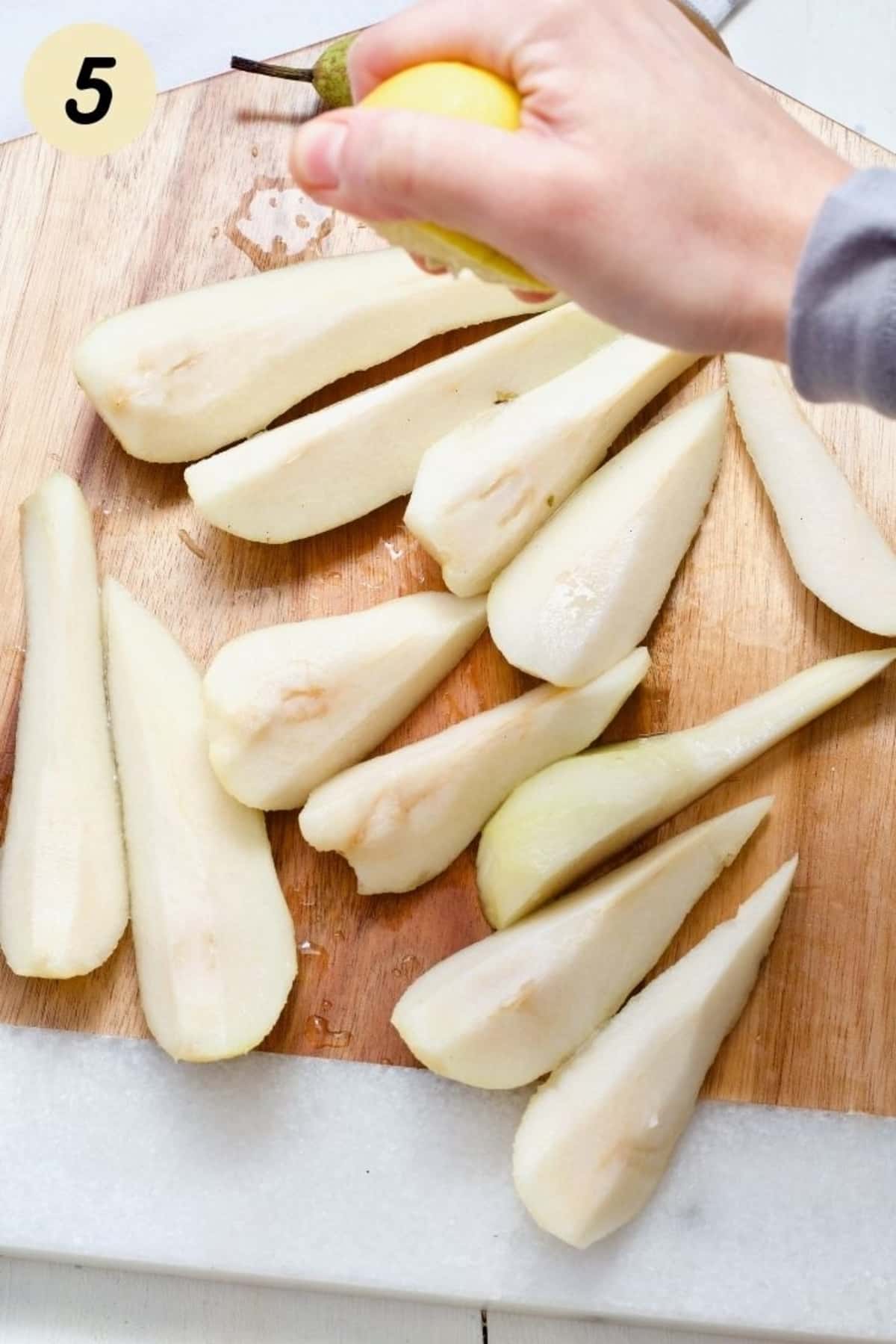 Lemon juice being squeezed out over peeled pears.