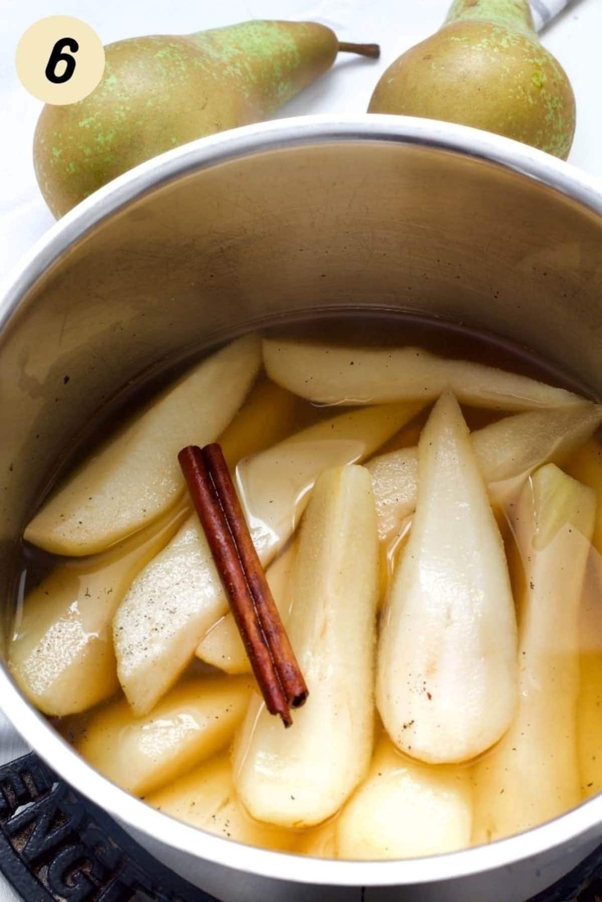 Pan with pears in cooking liquid with cinnamon stick.