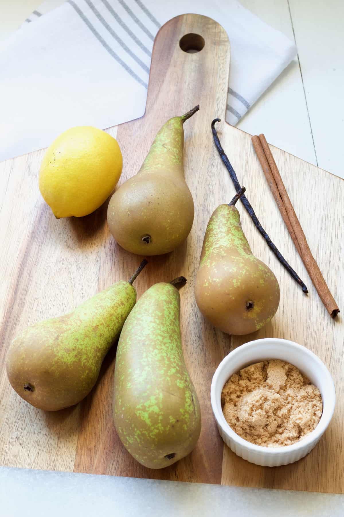 Pears, lemon, vanilla bean, cinnamon stick & brown sugar on a board.
