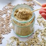 Spoon over jar with vegan parmesan, scattered sunflower and hemp seeds.