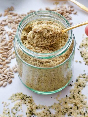 Spoon over jar with vegan parmesan, scattered sunflower and hemp seeds.