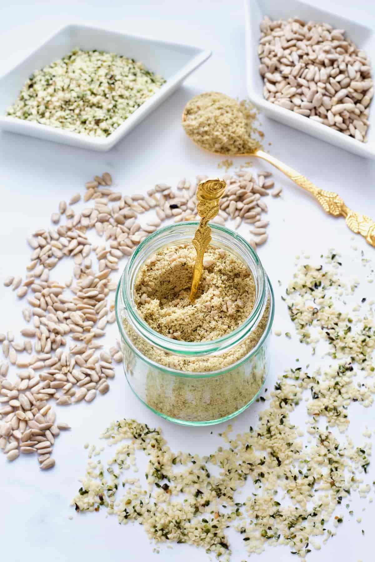 Jar with vegan parmesan, scattered seeds and seeds in dishes.