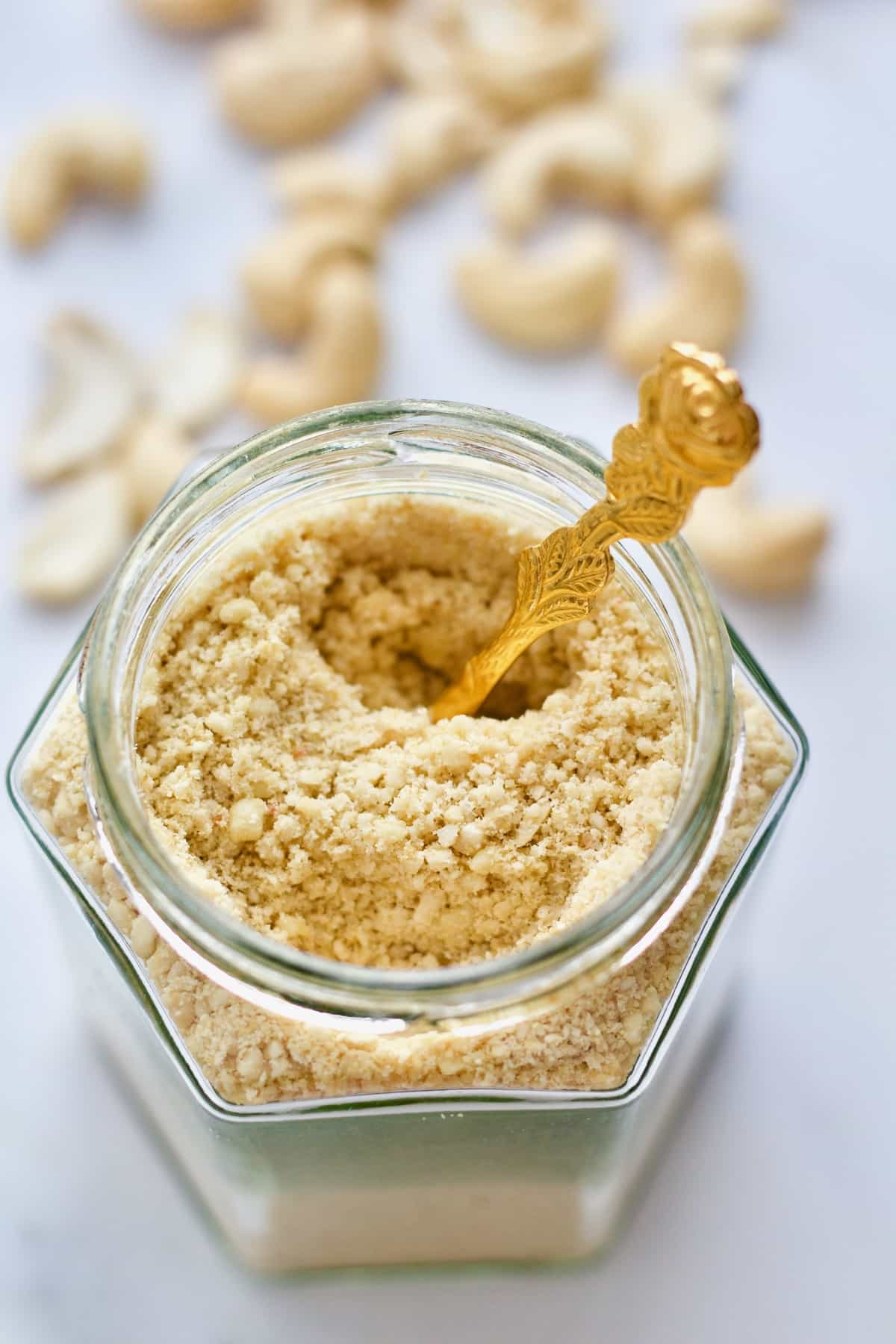 Close up of a jar with vegan cashew parmesan with a spoon in it.