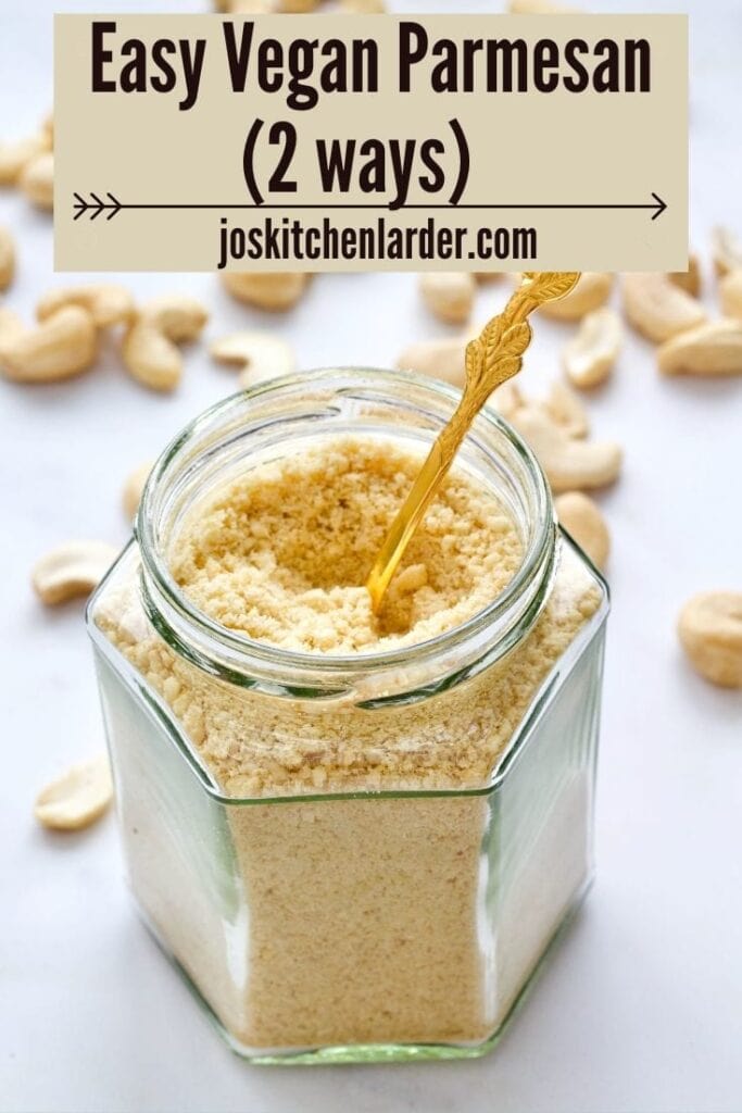 Jar with cashew vegan parmesan with spoon in it and cashews scattered around.