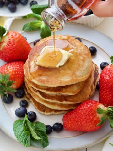 Plate with fluffy vegan buttermilk pancakes with vegan butter, maple and berries.