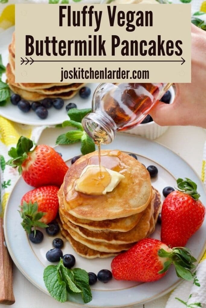 Maple syrup being poured over stack of fluffy vegan pancakes.