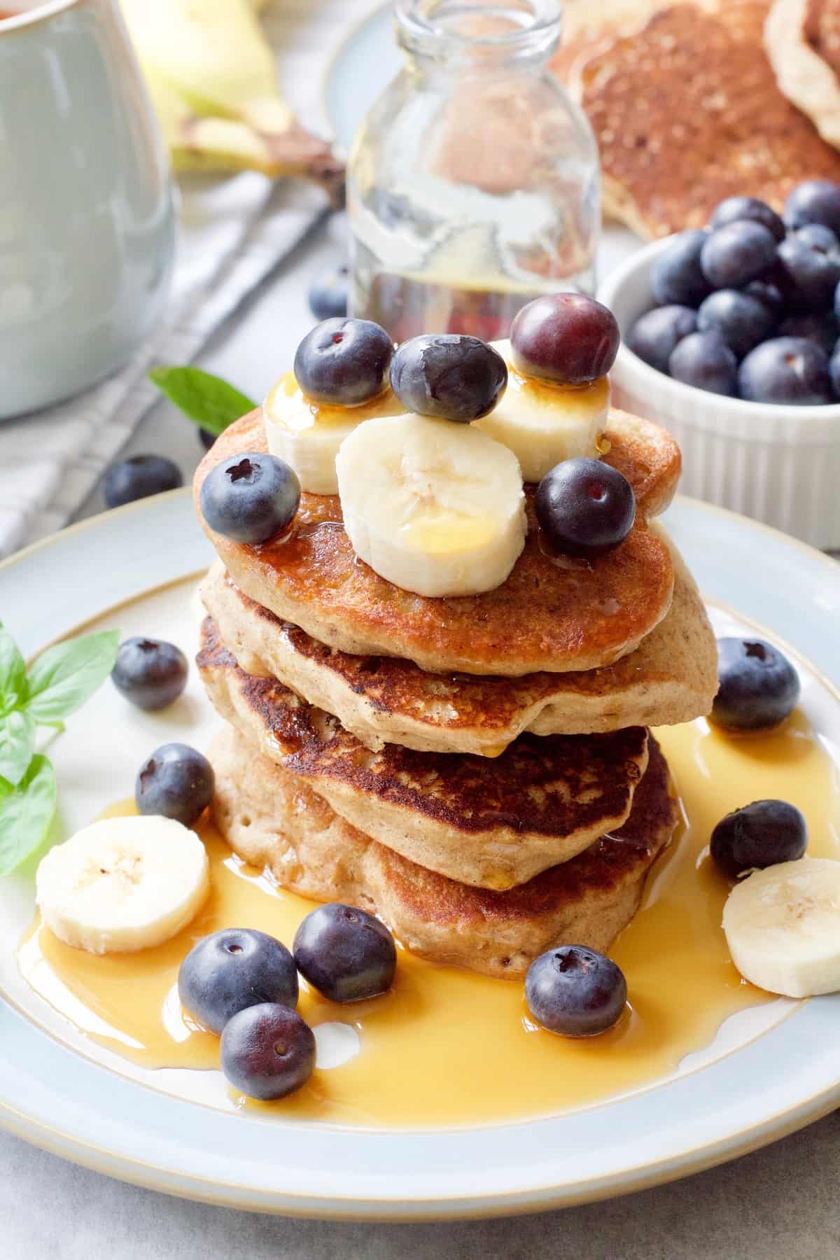 Stack of vegan buckwheat pancakes with fruits and maple syrup.