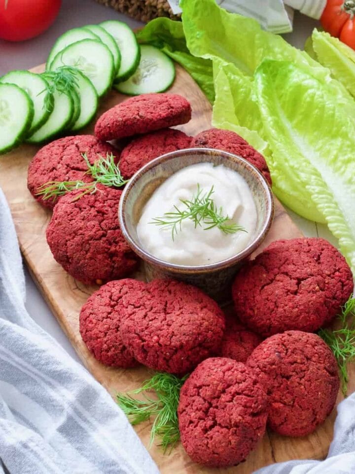 Beetroot falafel on a board with mayo dip in the middle, cucumber slices.