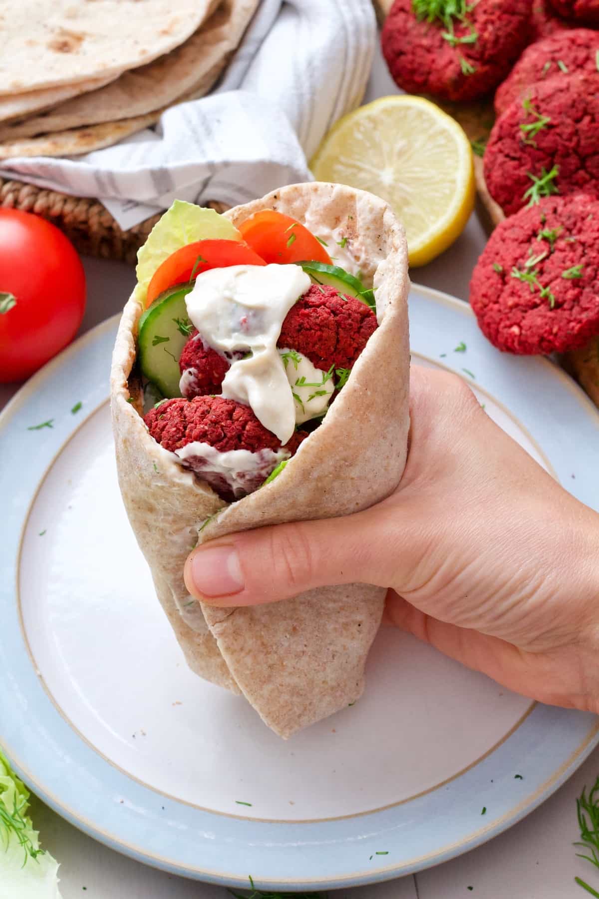 Hand holding flatbread stuffed with falafel and salad.