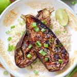 Miso-glazed aubergine halves served in a bowl on top of rice with lime and spring onions.