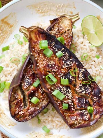 Miso-glazed aubergine halves served in a bowl on top of rice with lime and spring onions.