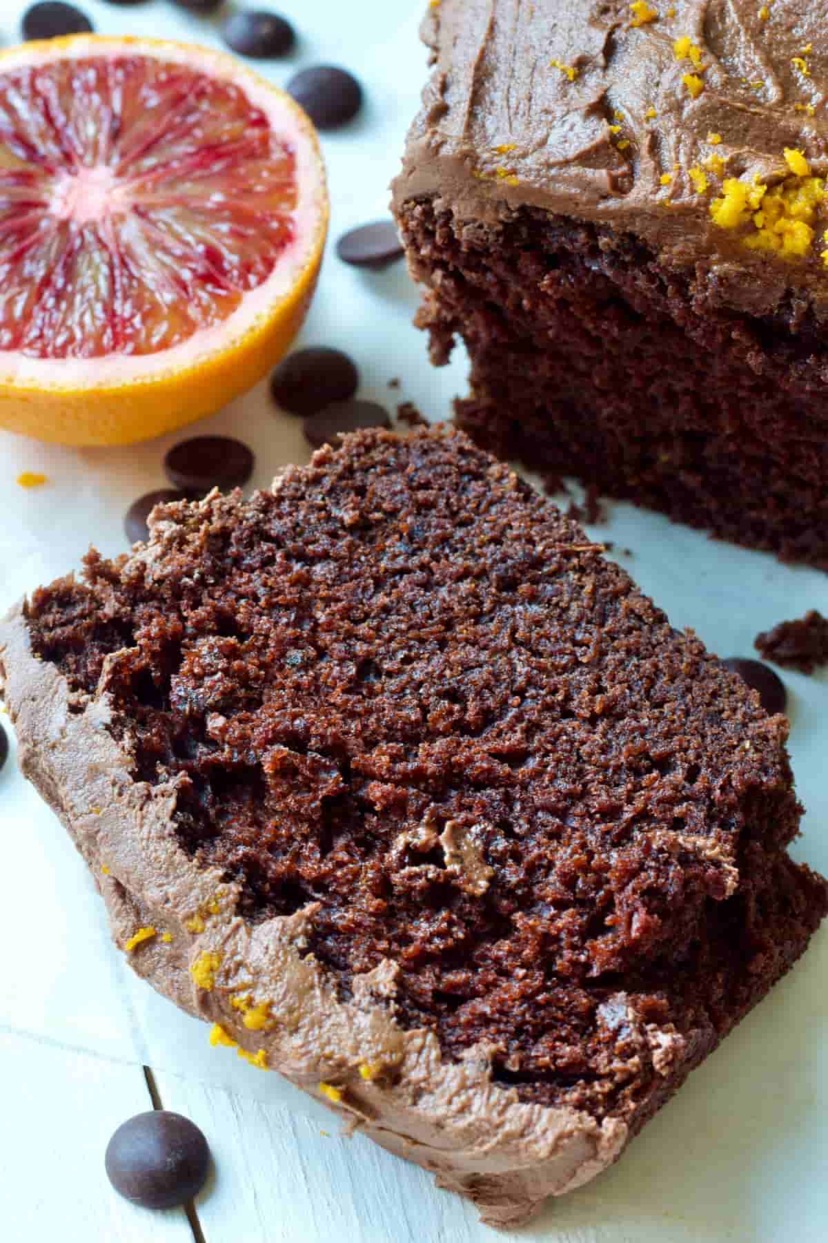 Slice of chocolate orange cake with orange half in the background.