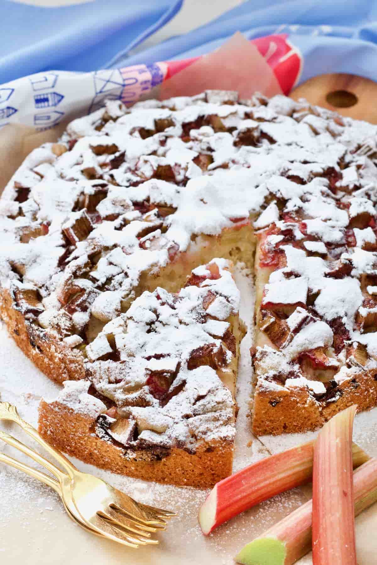 Easy rhubarb cake with a slice cut, dessert forks and pieces of raw rhubarb.