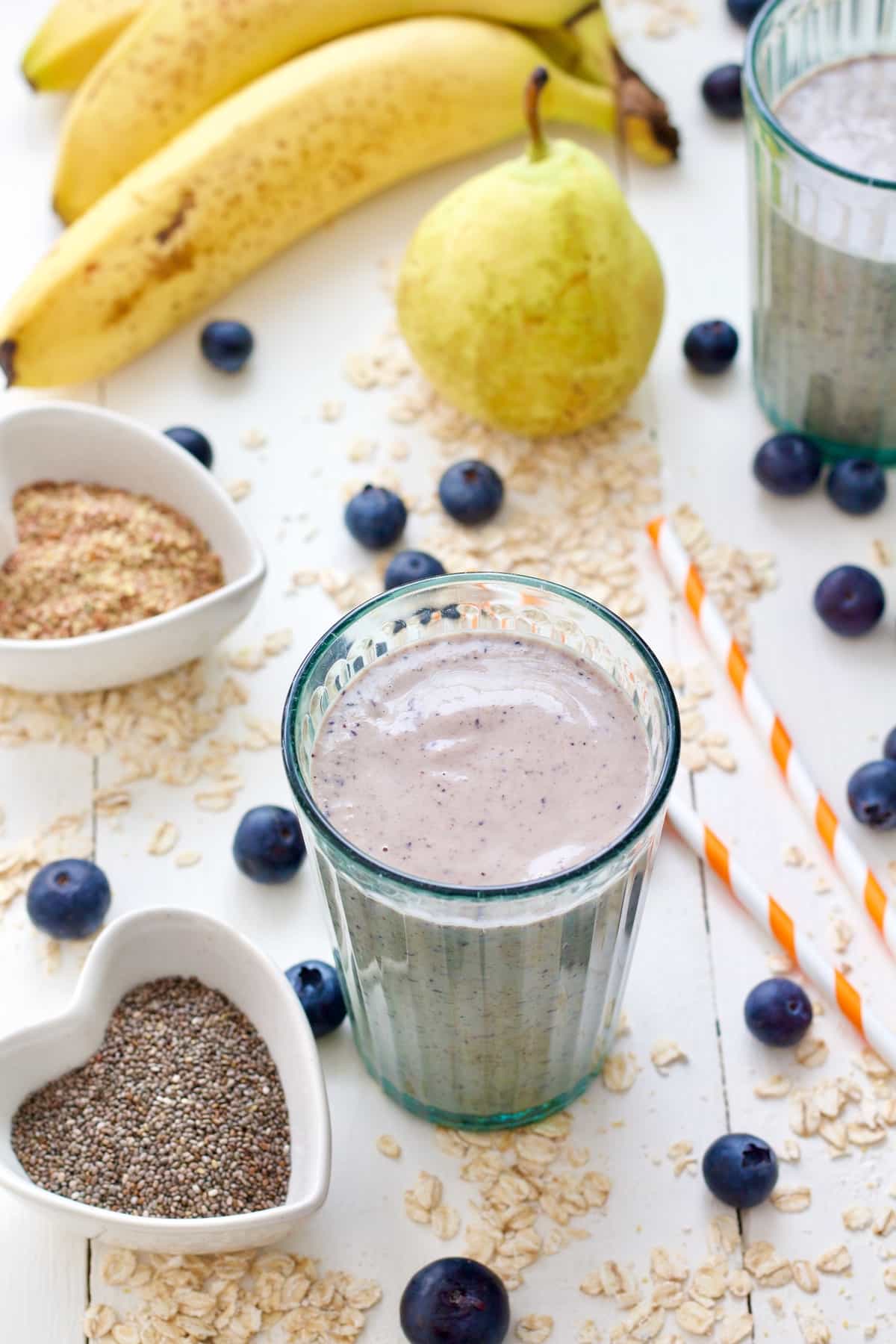 Glass with oat milk smoothies with oats & blueberries scattered around it.