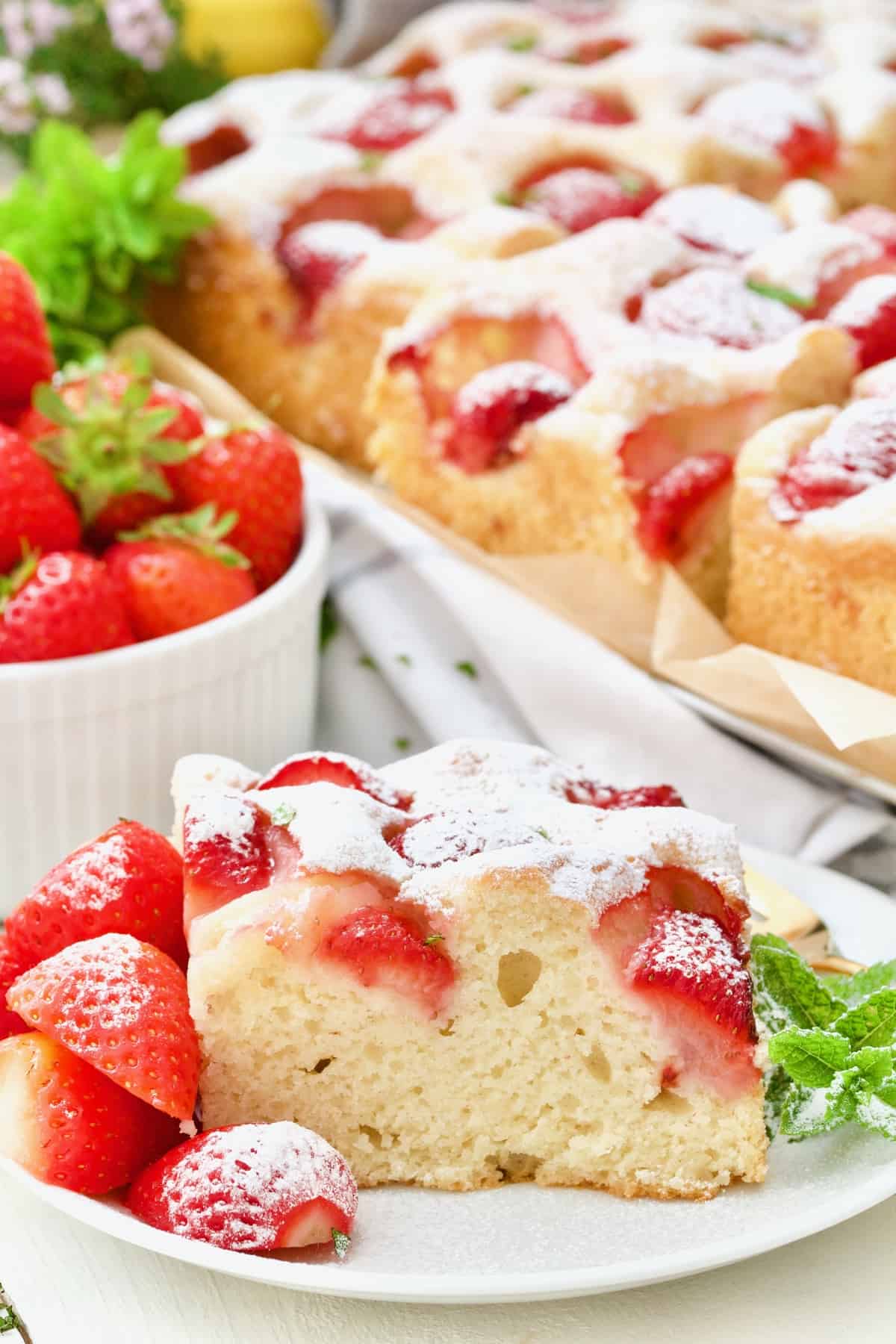 Serving of strawberry cake with whole cake in the background.