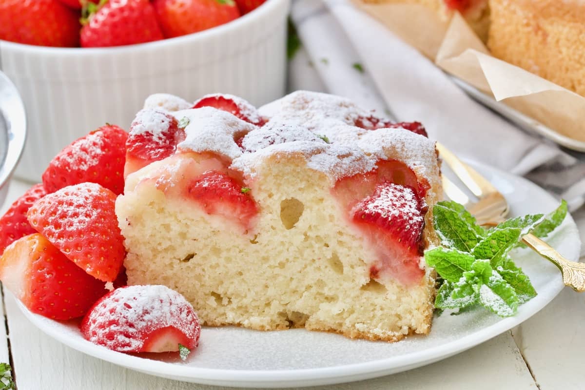 Portion of strawberry yogurt cake on a plate with mint and strawberries.