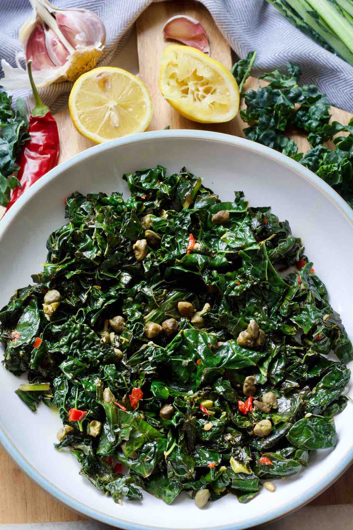 Plate with stir fried black kale, chilli, lemons, garlic around it.