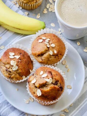 Close up of three banana muffins on a plate, coffee and a banana.
