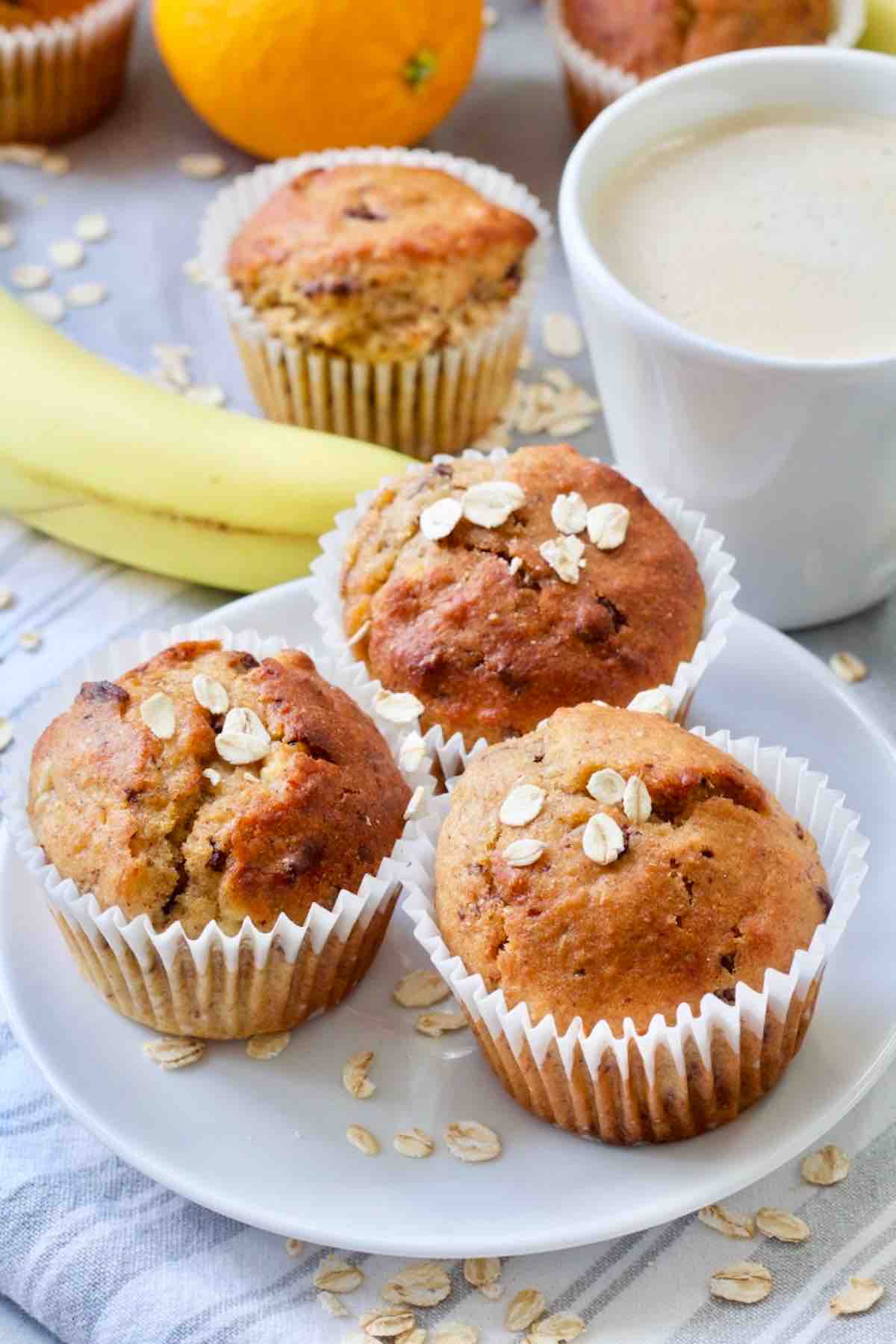 Three vegan banana muffins on a plate with coffee behind.