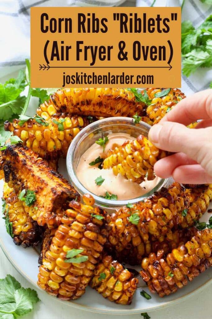 Hand dunking corn rib in a bowl with a dip.