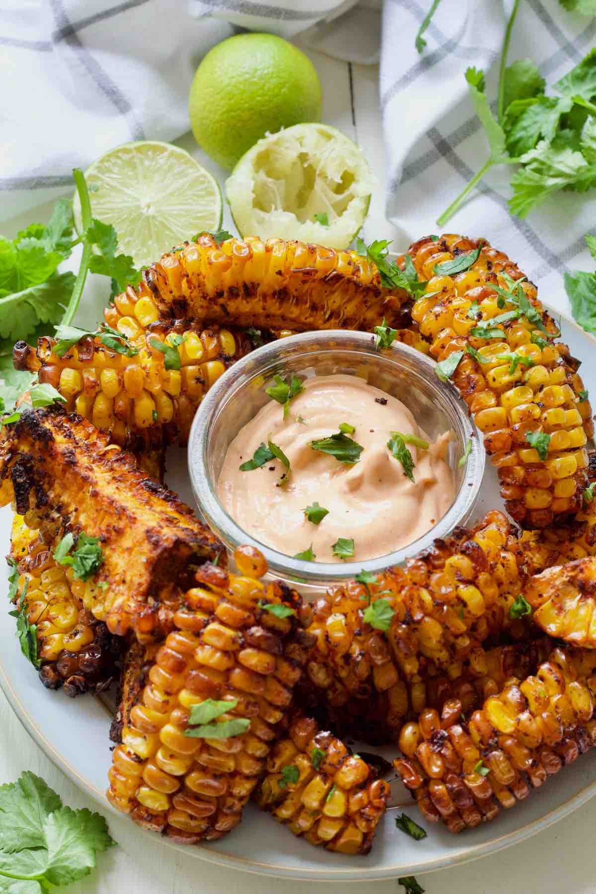 Plate with corn ribs, dip, limes and coriander around it.