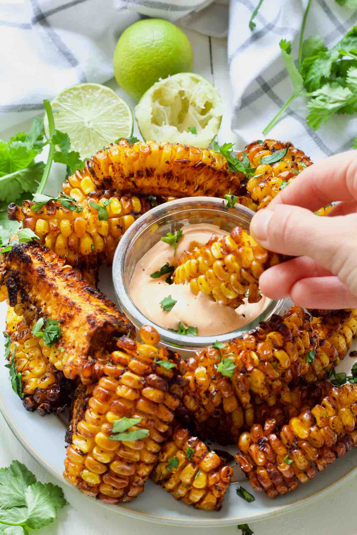 Hand dunking corn rib in a bowl with a dip.