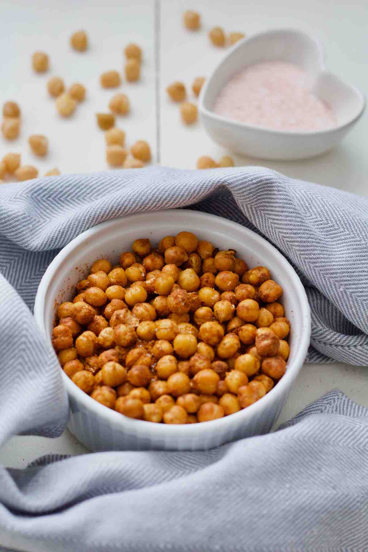 Air fryer chickpeas in a bowl, more chickpeas behind and salt in a pinch bowl.