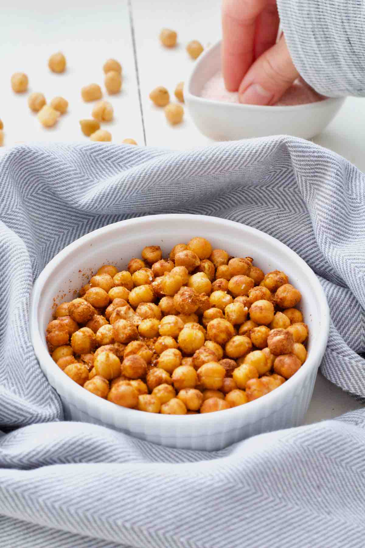 Air fryer chickpeas in a bowl, hand taking a pinch of salt behind it.