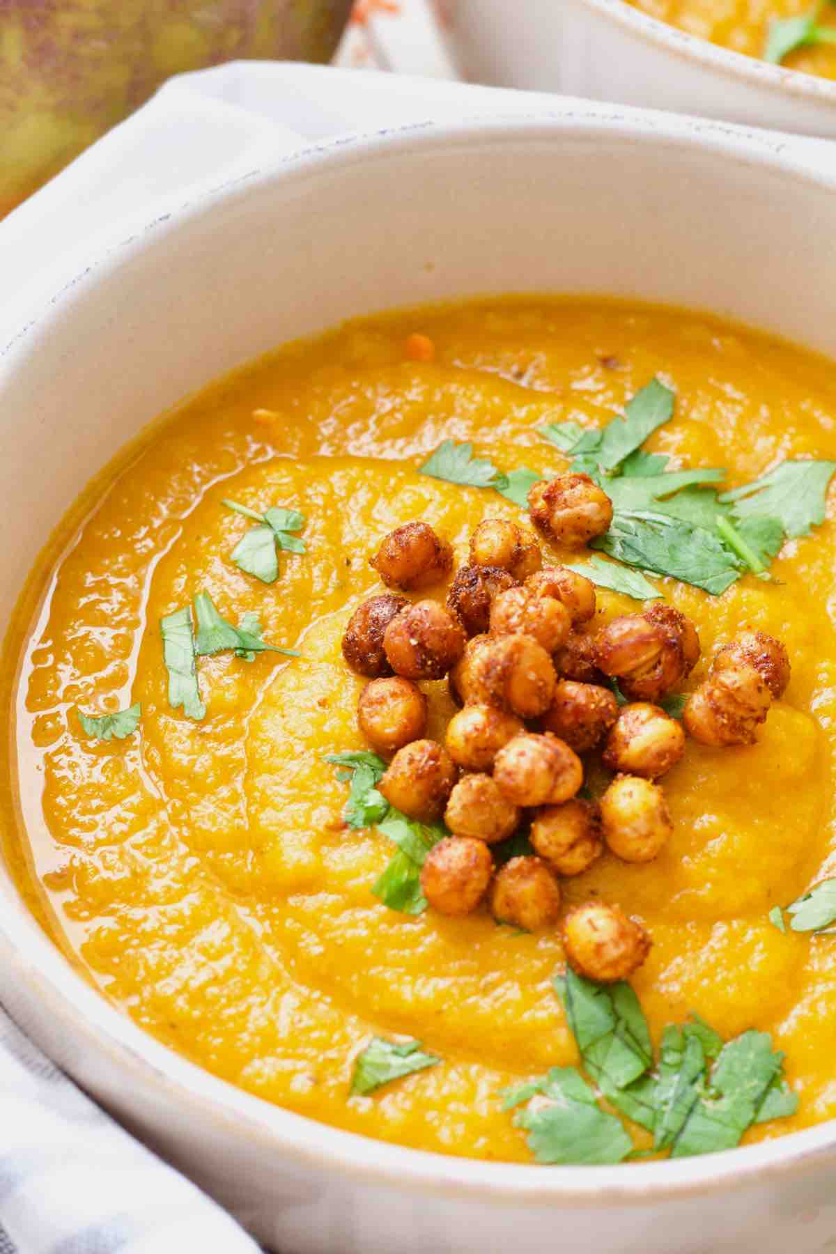 Close up of carrot and swede soup in a bowl garnished with chickpeas and coriander.