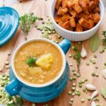 Vegan split pea soup in a bowl, tempeh cubes, garlic, herbs, split peas scattered around.