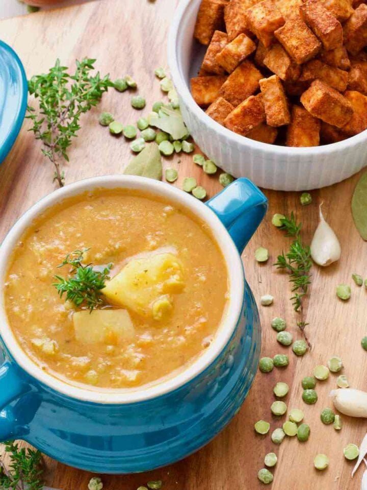 Vegan split pea soup in a bowl, tempeh cubes, garlic, herbs, split peas scattered around.